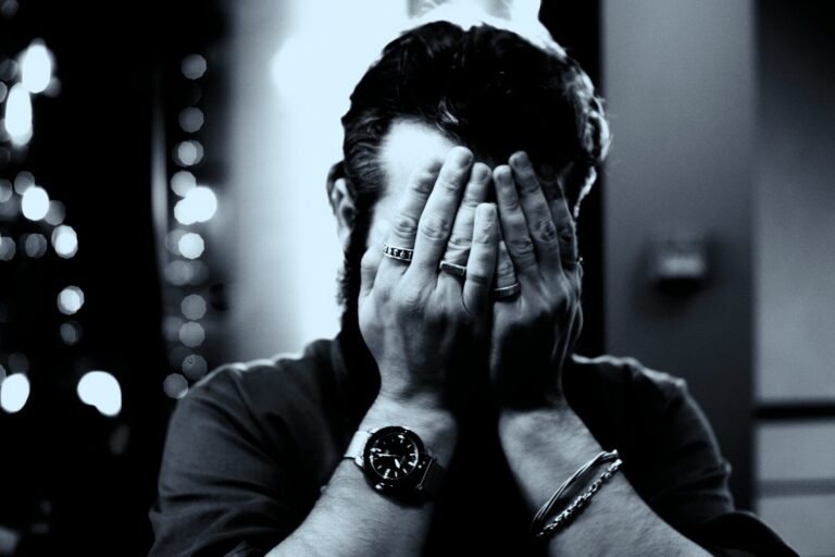 A person covers their face with hands, wearing a watch
