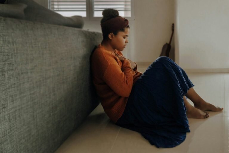A woman in an orange sweater and blue skirt sitting on the floor